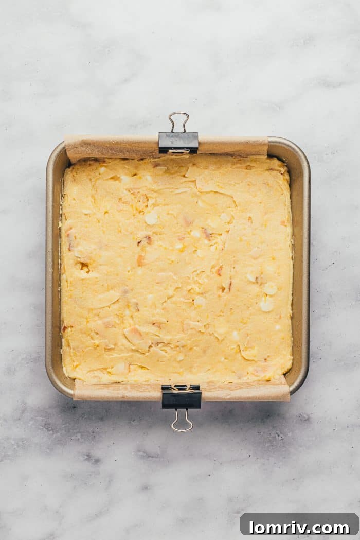 An 8-inch baking tray filled with unbaked lemon blondie batter, evenly spread and ready for the oven.