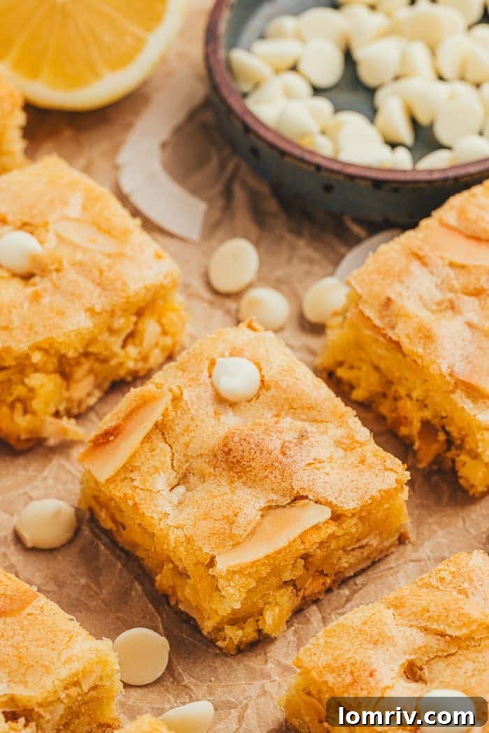 Lemon blondies perfectly cut into bars, adorned with white chocolate chips on a rustic surface.