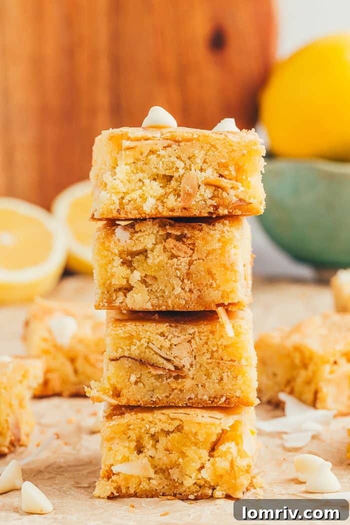 A charming stack of golden lemon blondies, with vibrant half-cut lemons in the soft-focus background.