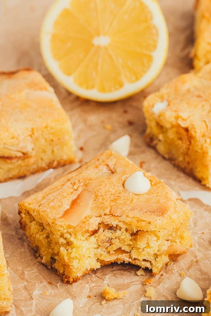 A close-up of a lemon blondie with a bite taken out, revealing its soft and chewy interior with visible coconut flakes and white chocolate chips.