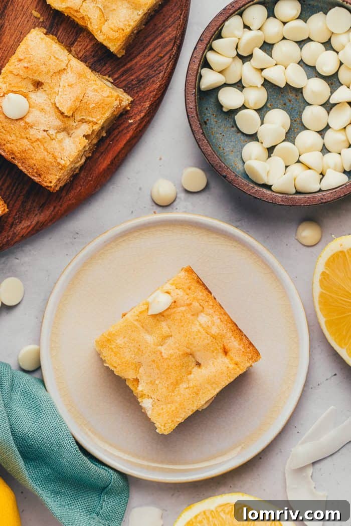 A single lemon blondie resting on a small white plate, with a bowl of white chocolate chips in the background.