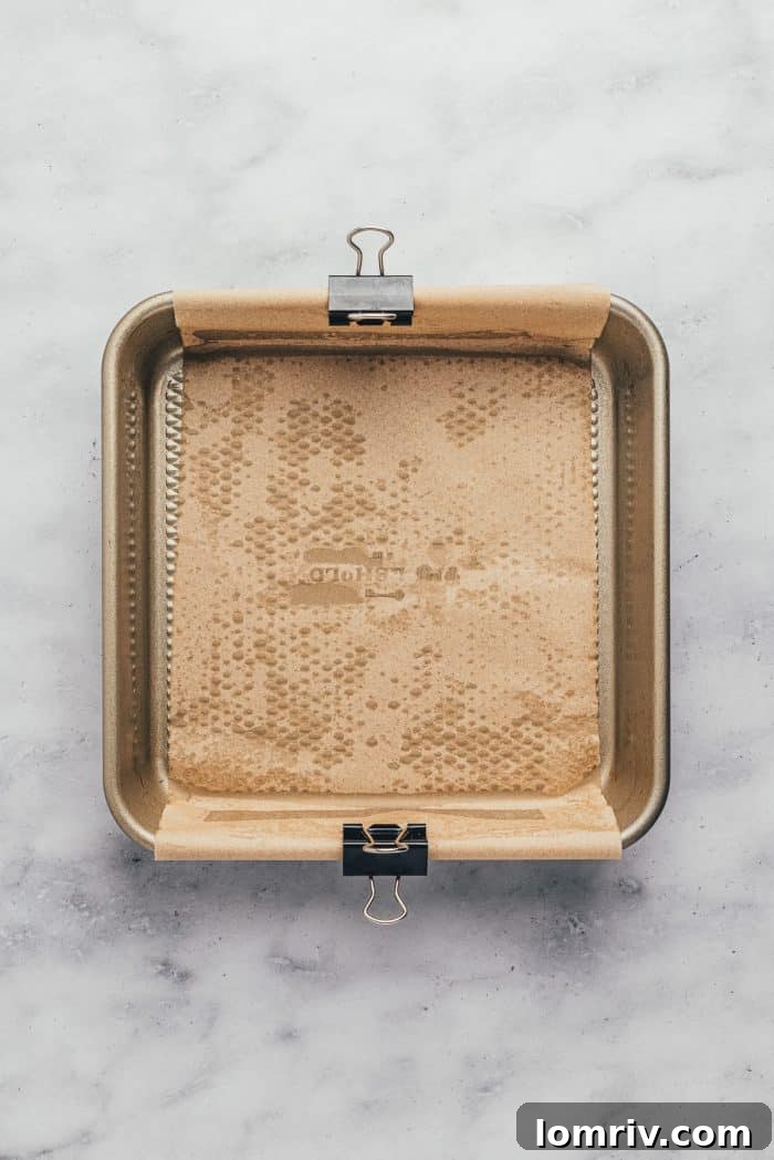 A square baking pan meticulously lined with parchment paper, ready for the blondie batter.