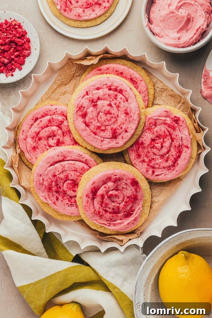 Vibrant lemon sugar cookies with pink raspberry cream cheese frosting in a white dish, garnished with fresh lemon slices and raspberries.
