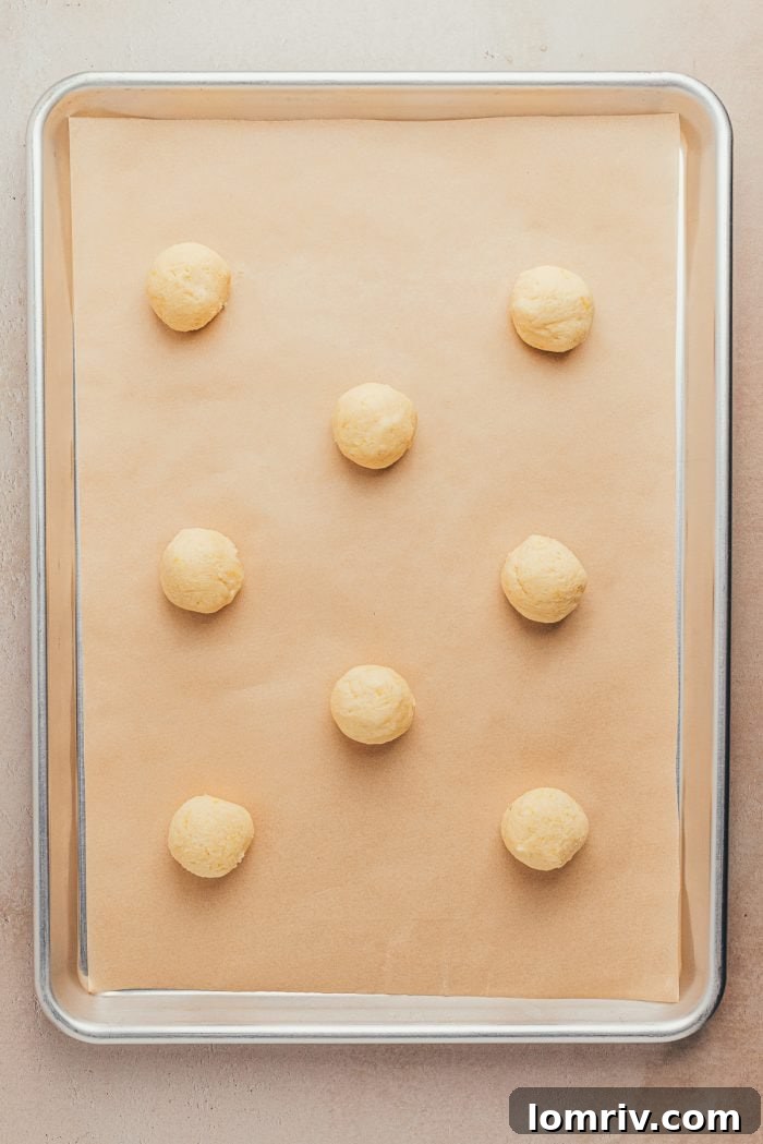 A baking sheet with neatly spaced, unbaked lemon sugar cookie dough balls on parchment paper.
