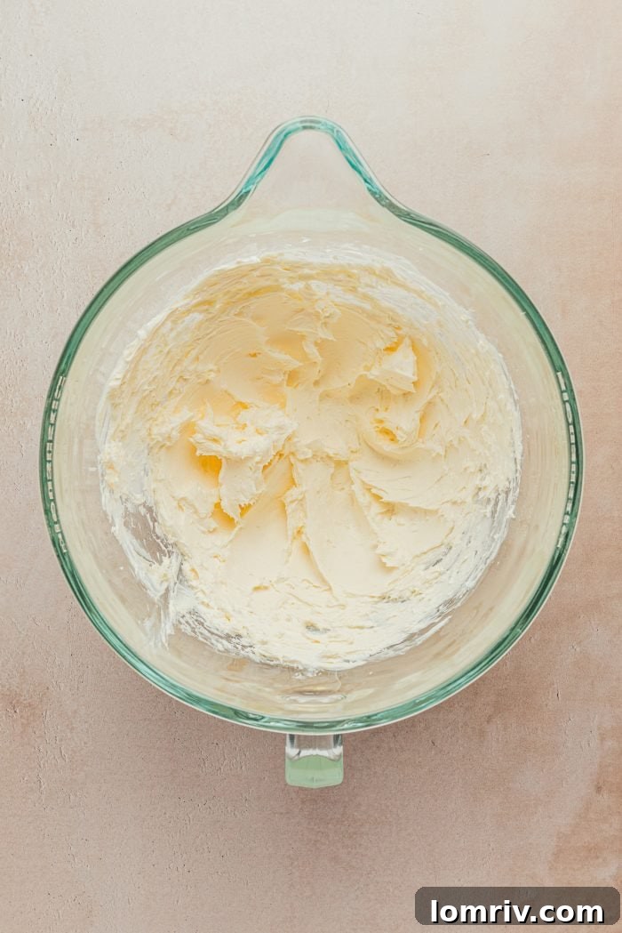 Softened butter and cream cheese mixed together in a clear glass bowl, forming a smooth base for the frosting.