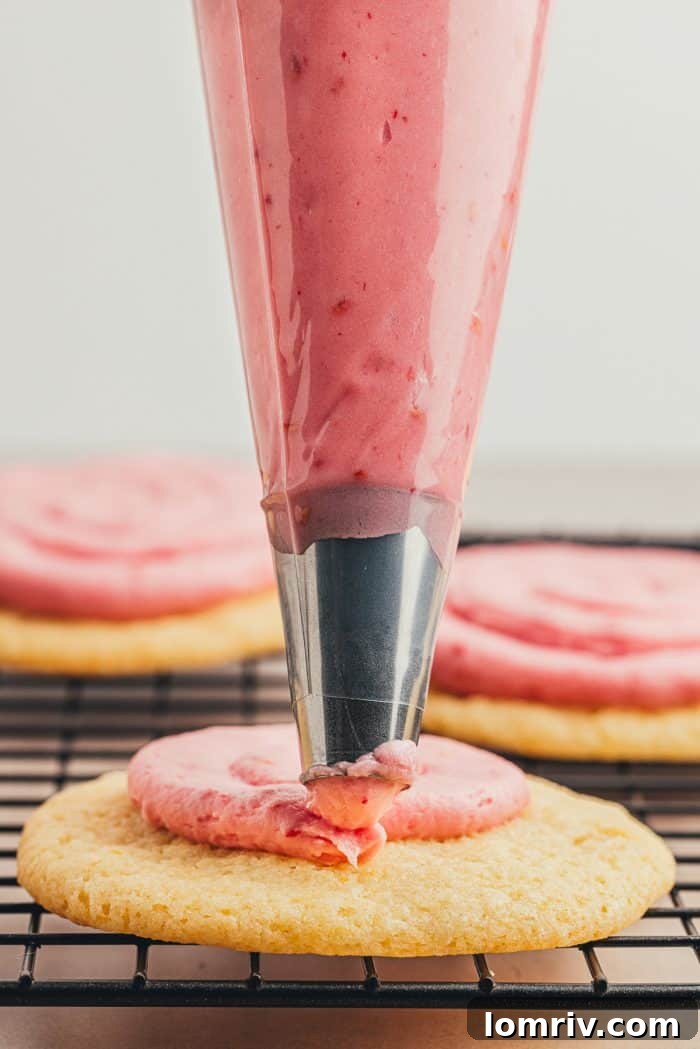 A piping bag expertly decorating a sugar cookie with delicate swirls of pink raspberry frosting.