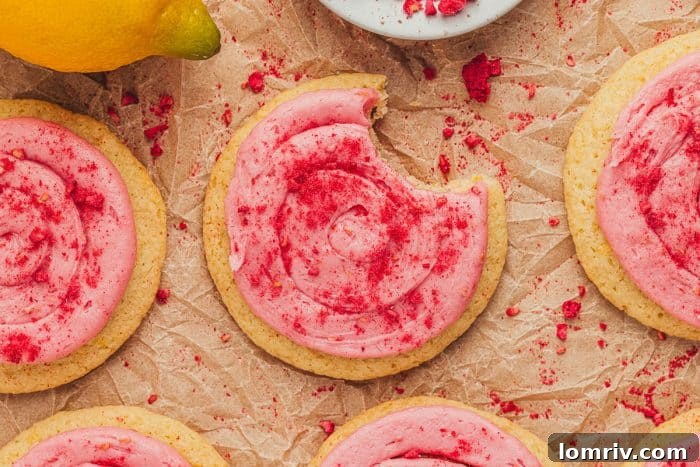 Lemon sugar cookies with raspberry cream cheese frosting artfully arranged on parchment paper, ready for serving.