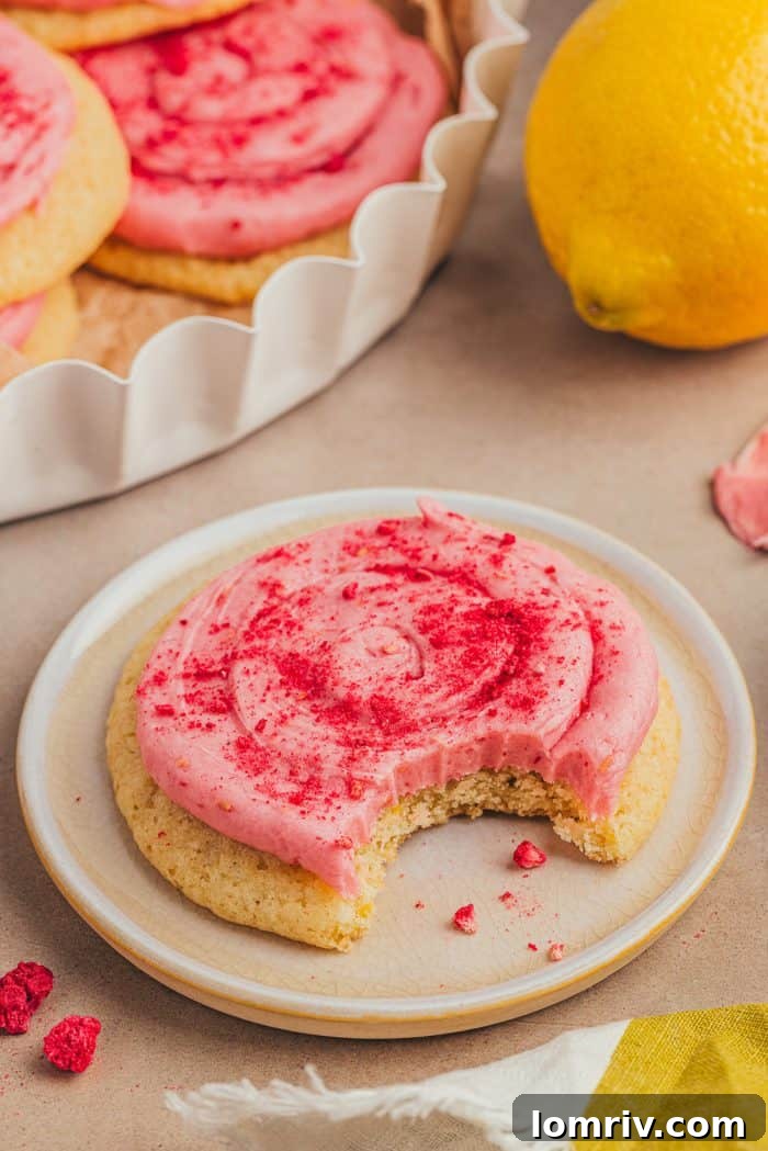 A single perfectly frosted lemon sugar cookie resting on a crisp white plate, showcasing its soft texture and inviting pink frosting.