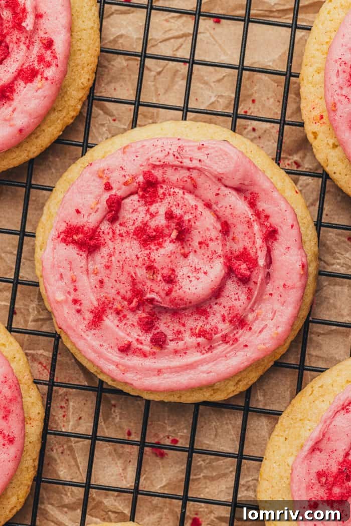 Close-up view of multiple lemon sugar cookies adorned with delicate swirls of raspberry cream cheese frosting, arranged on a rustic surface.