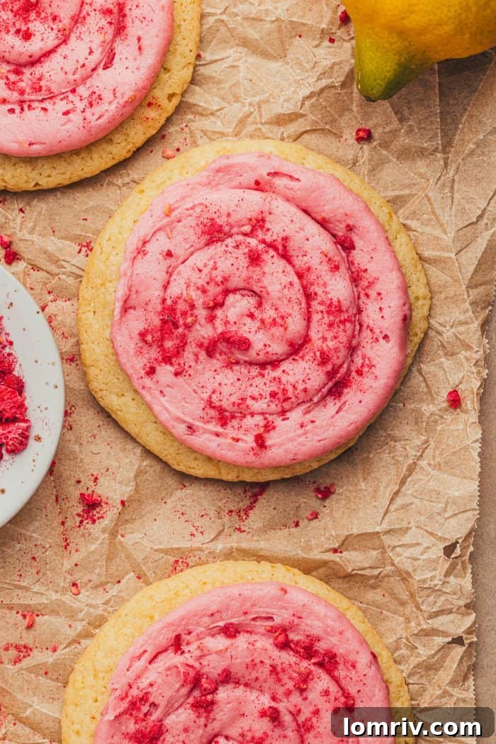 An array of lemon sugar cookies with raspberry cream cheese frosting resting on parchment paper after being decorated.