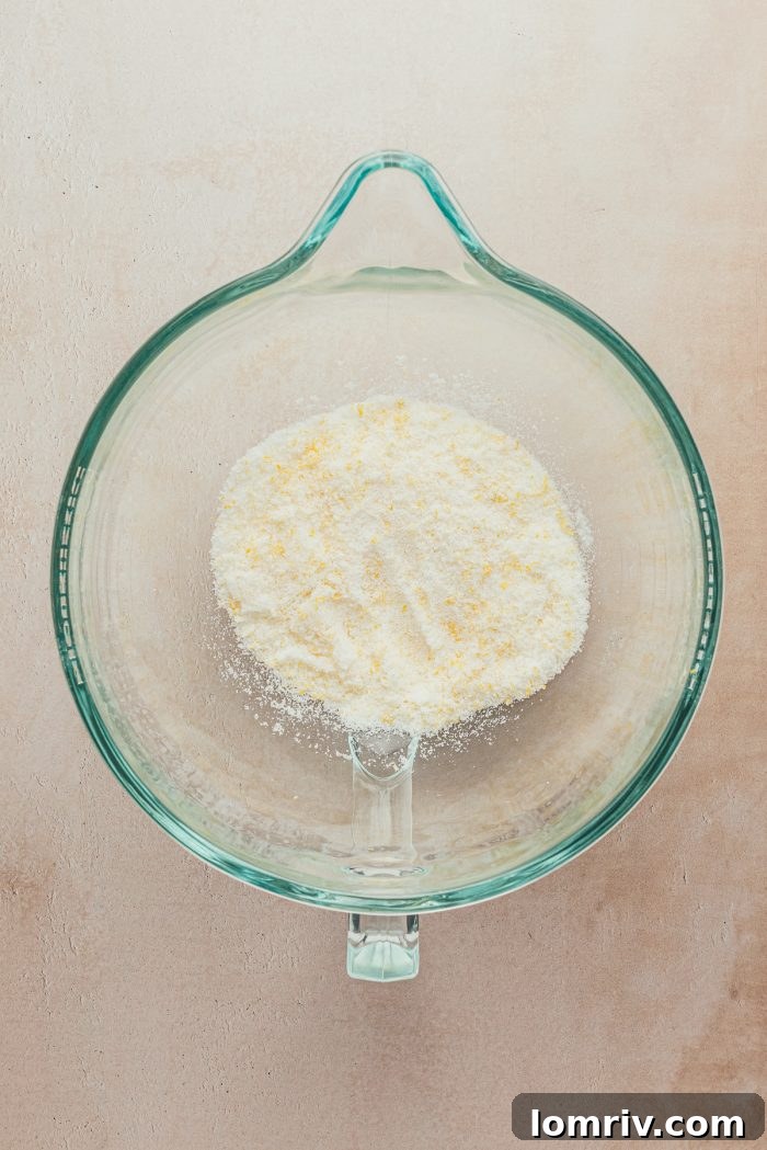 A glass bowl containing white granulated sugar infused with bright yellow lemon zest.