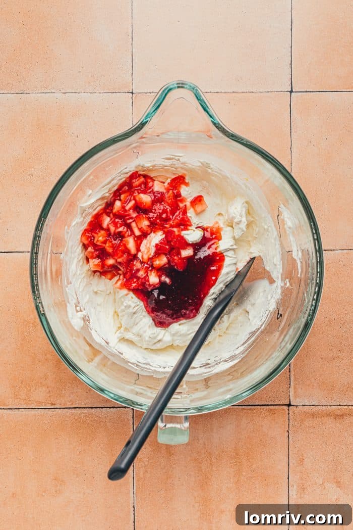Diced strawberries over the whipped heavy cream mixture with a black spatula in a glass bowl.
