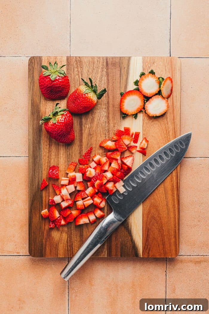 Diced strawberries with a knife on a wooden cutting board.