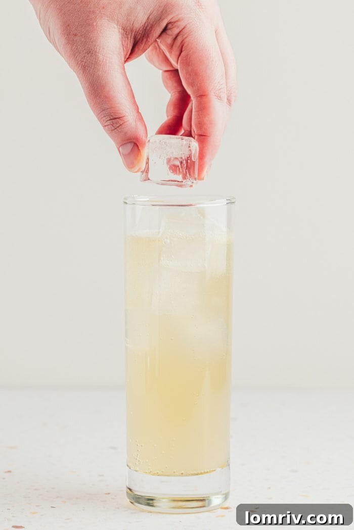 Ice cubes being carefully added to a tall glass of lemon elderflower mocktail.