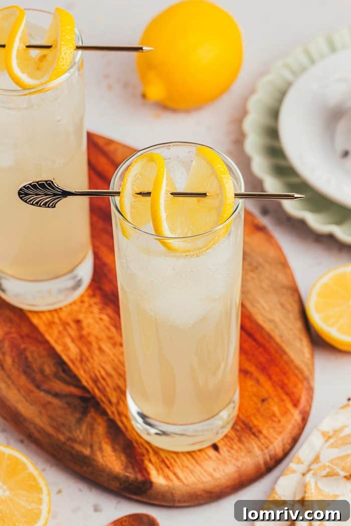 Two tall glasses of lemon elderflower mocktail, garnished with lemon slices, sitting on a rustic wooden board.