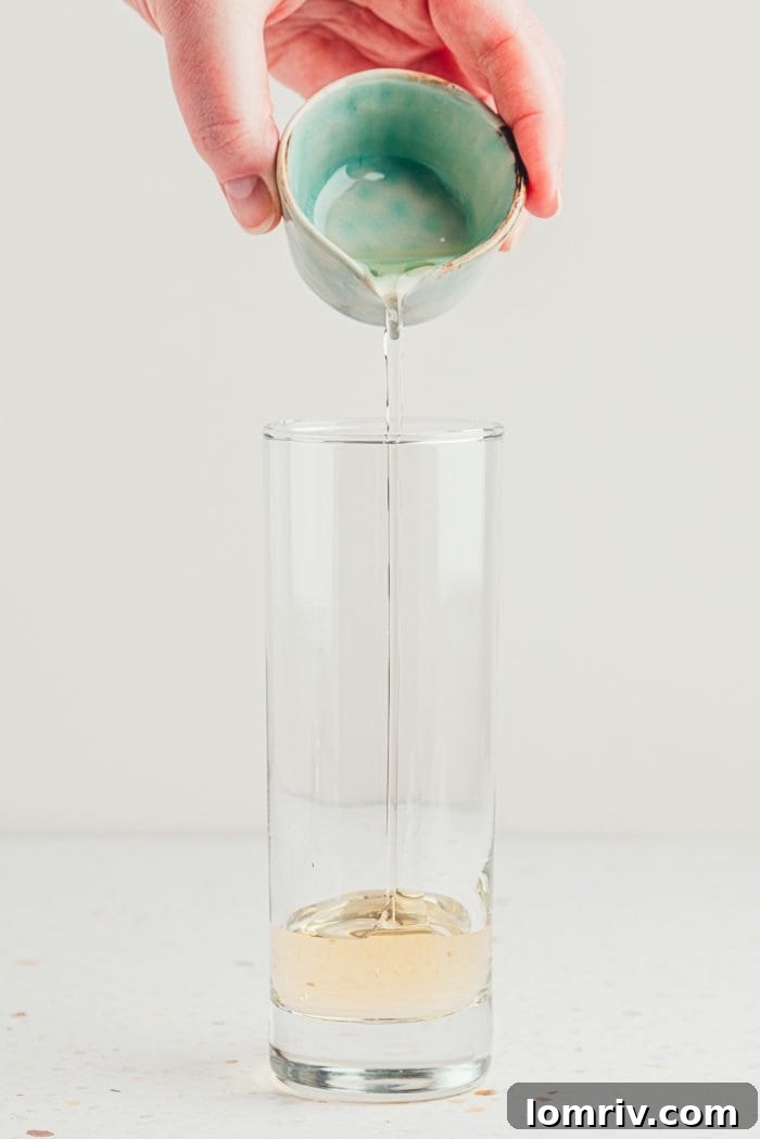 Pouring elderflower cordial into a tall glass, the first step in making a delicious mocktail.