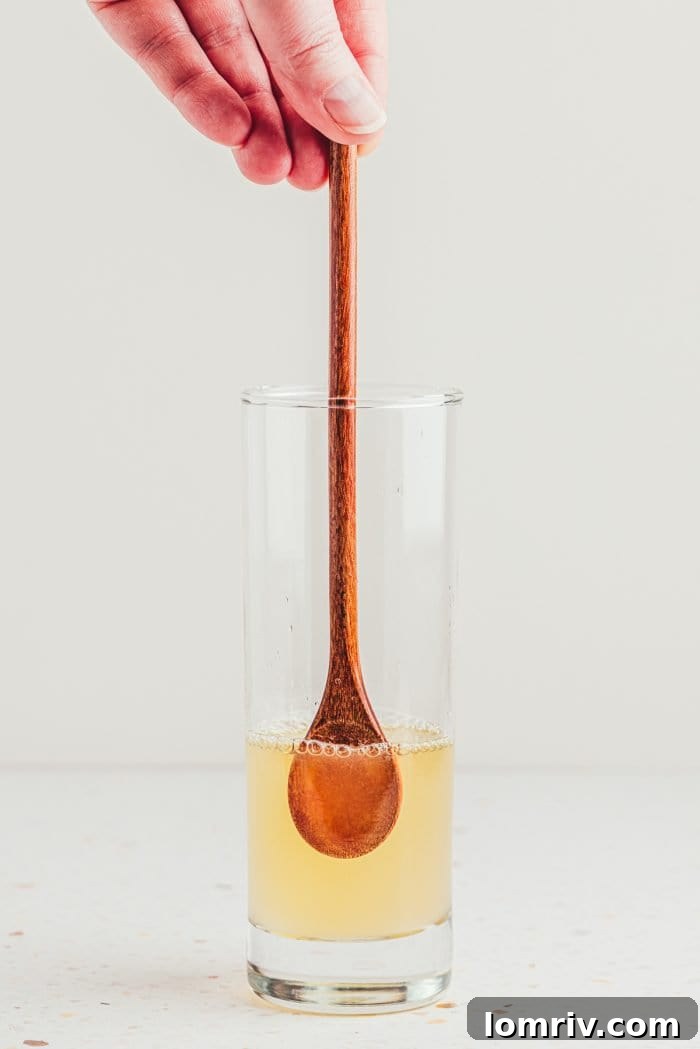 A wooden spoon stirring the ingredients in a tall glass, ensuring a well-mixed lemon elderflower mocktail base.