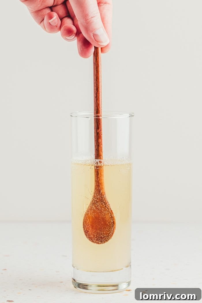 A wooden spoon gently stirring the finished lemon elderflower mocktail in a tall glass.