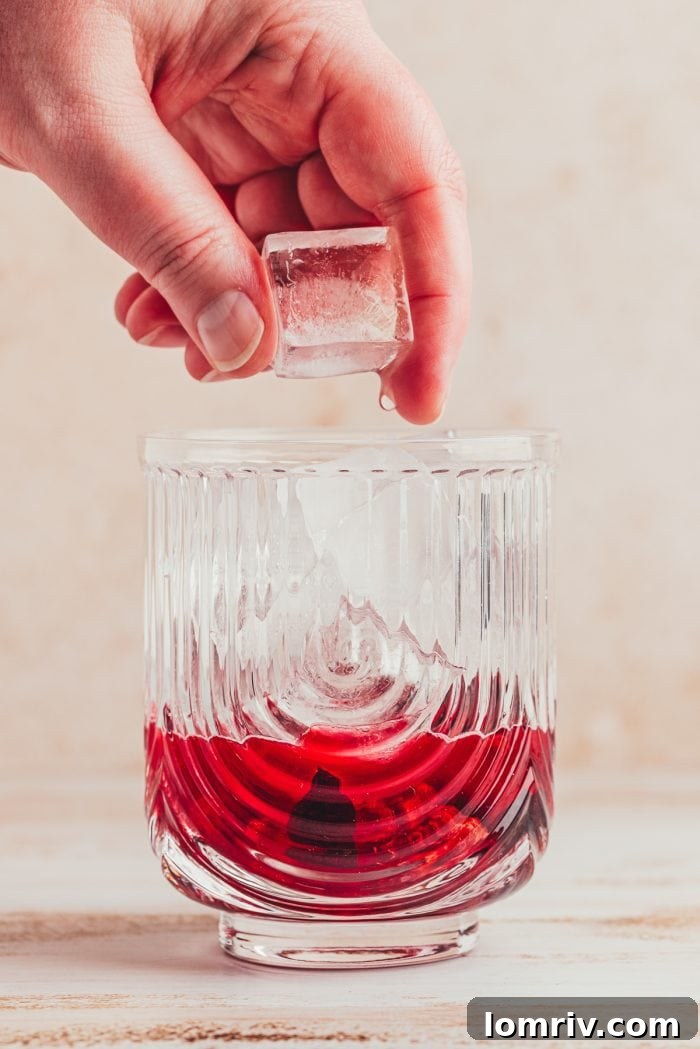 Ice being added to the glass filled with cherries and lime juice.