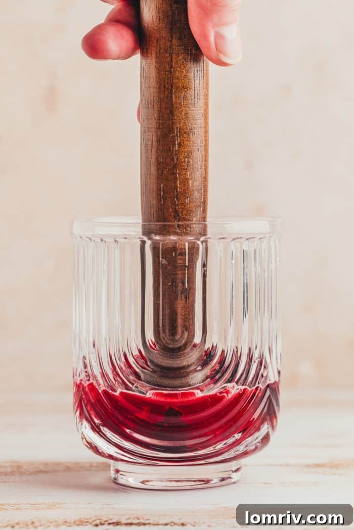 Cherries being muddled with a muddle stick in a glass.
