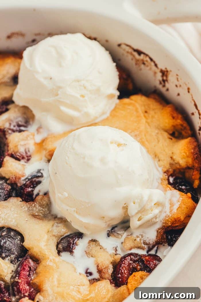 An oval baking dish with cherry cobbler and two scoops of ice cream.