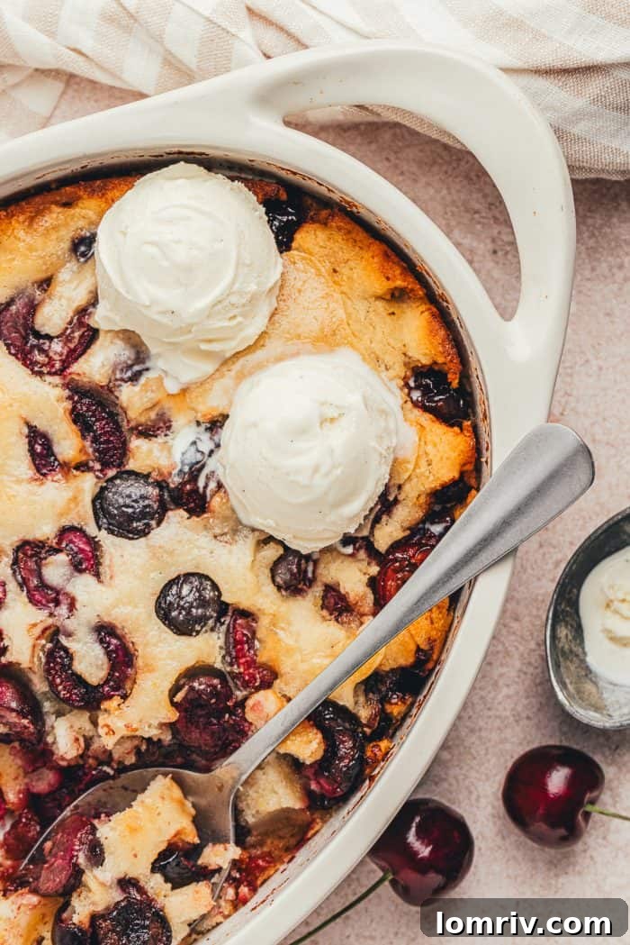 An oval baking dish with cherry cobbler and two scoops of ice cream.