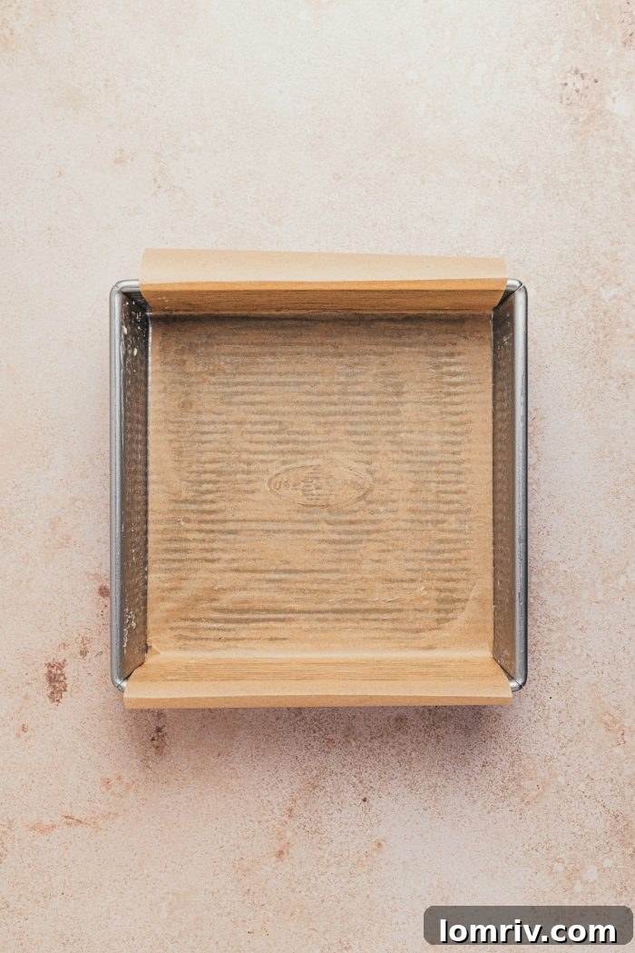 A greased baking pan lined with parchment paper, prepared for the cake batter.