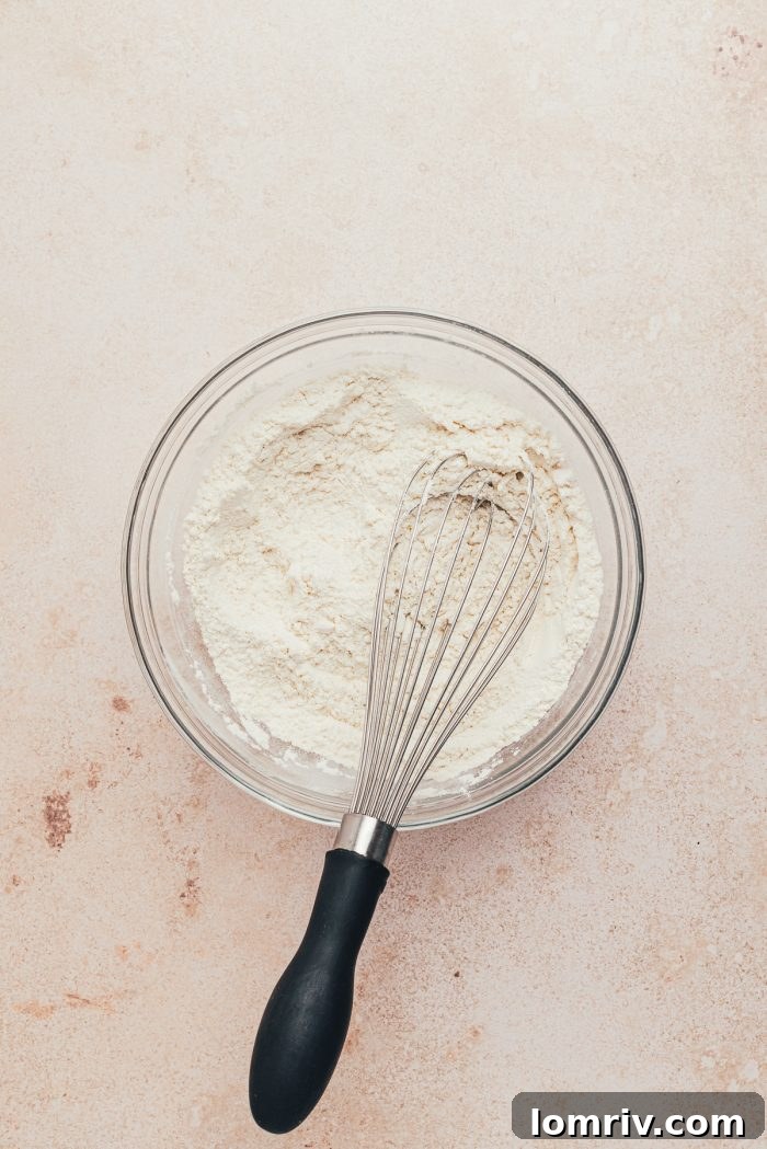 Dry ingredients (flour, baking powder, salt) being whisked together in a glass bowl.