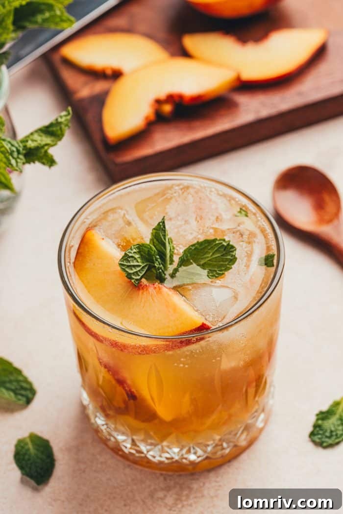 A glass filled with a bourbon peach smash and a wooden board with sliced peaches in the background.