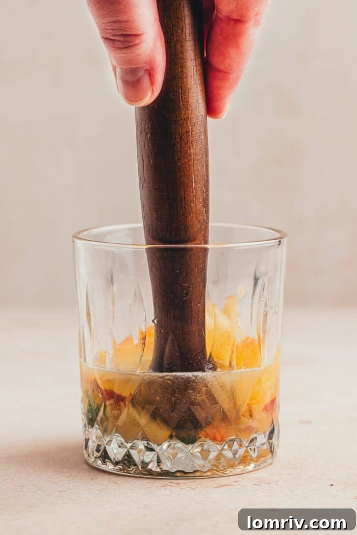 Peaches being muddled in a glass.