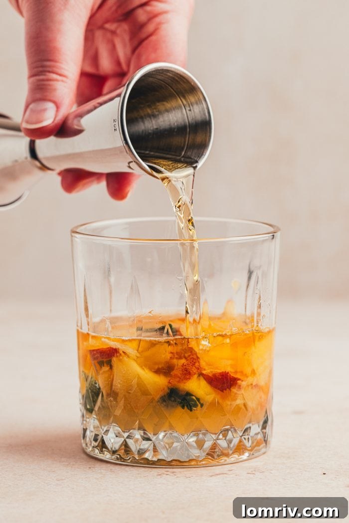Bourbon being poured into a glass with sliced peaches.