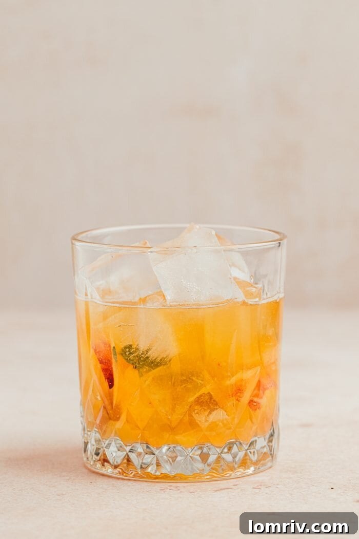 Ice being added to a glass of peach bourbon smash.