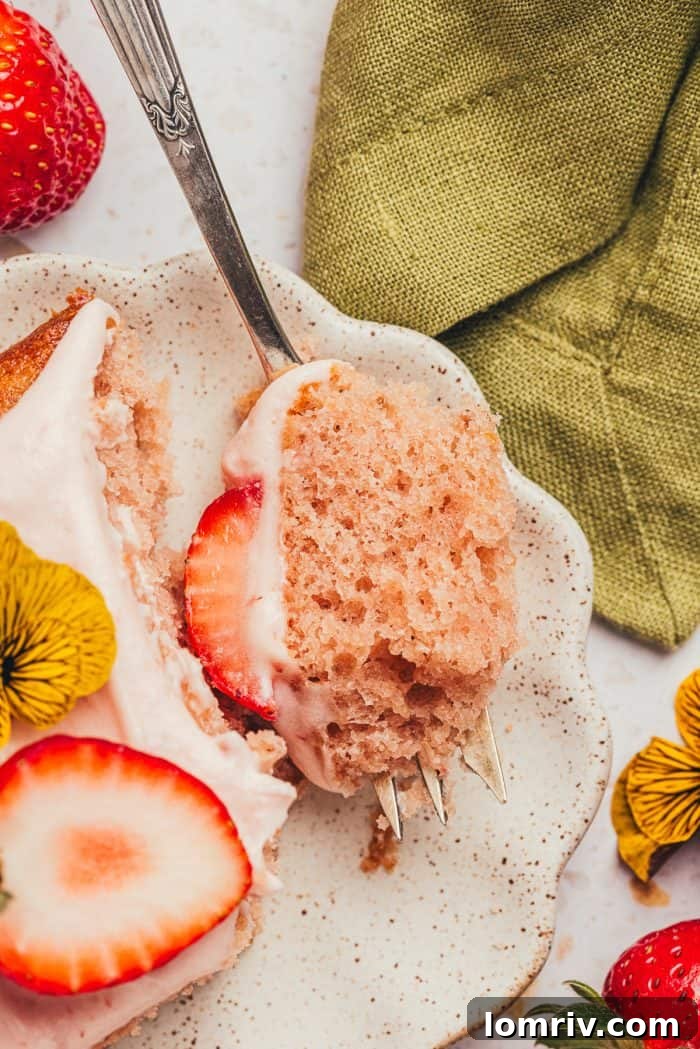 A slice of strawberry sheet cake on a plate, a fork gently piercing into its soft, frosted surface