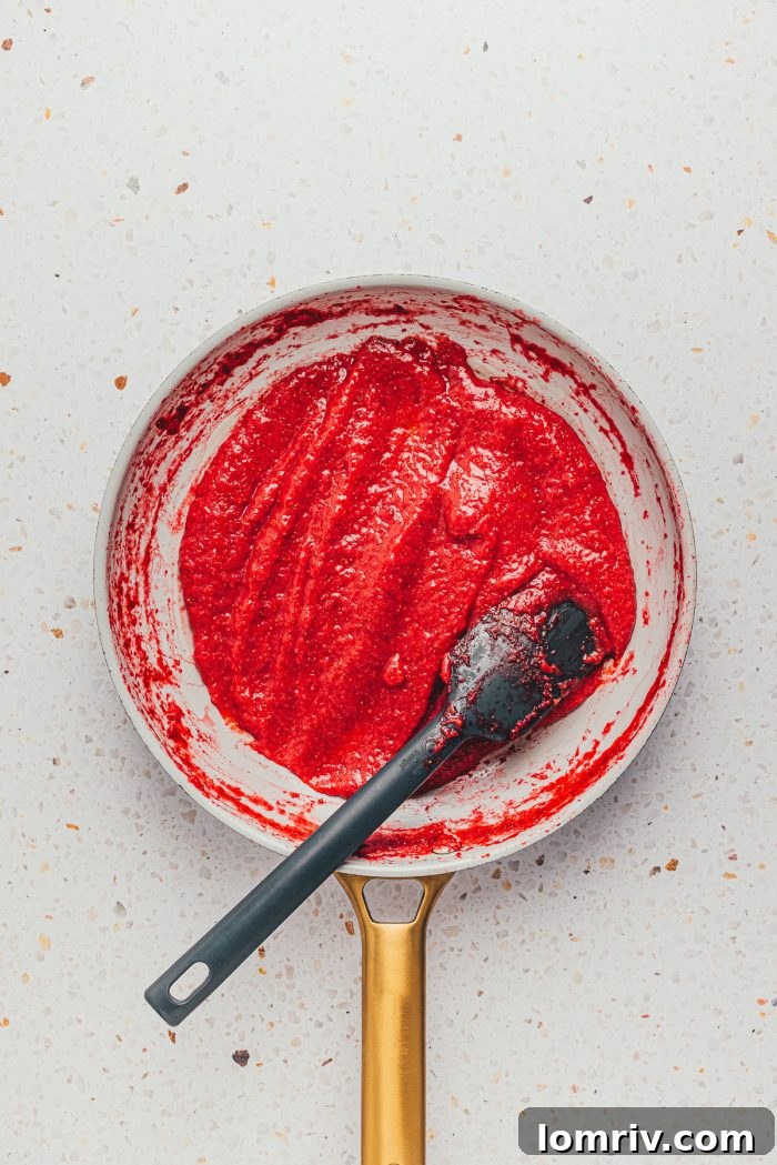 Strawberry puree actively reducing in a skillet on the stovetop, concentrating its sweet flavor
