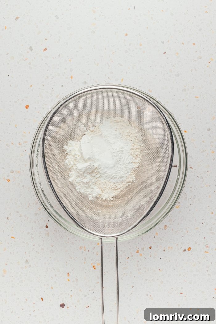 Dry ingredients being sifted into a glass bowl, ensuring a smooth and lump-free cake batter