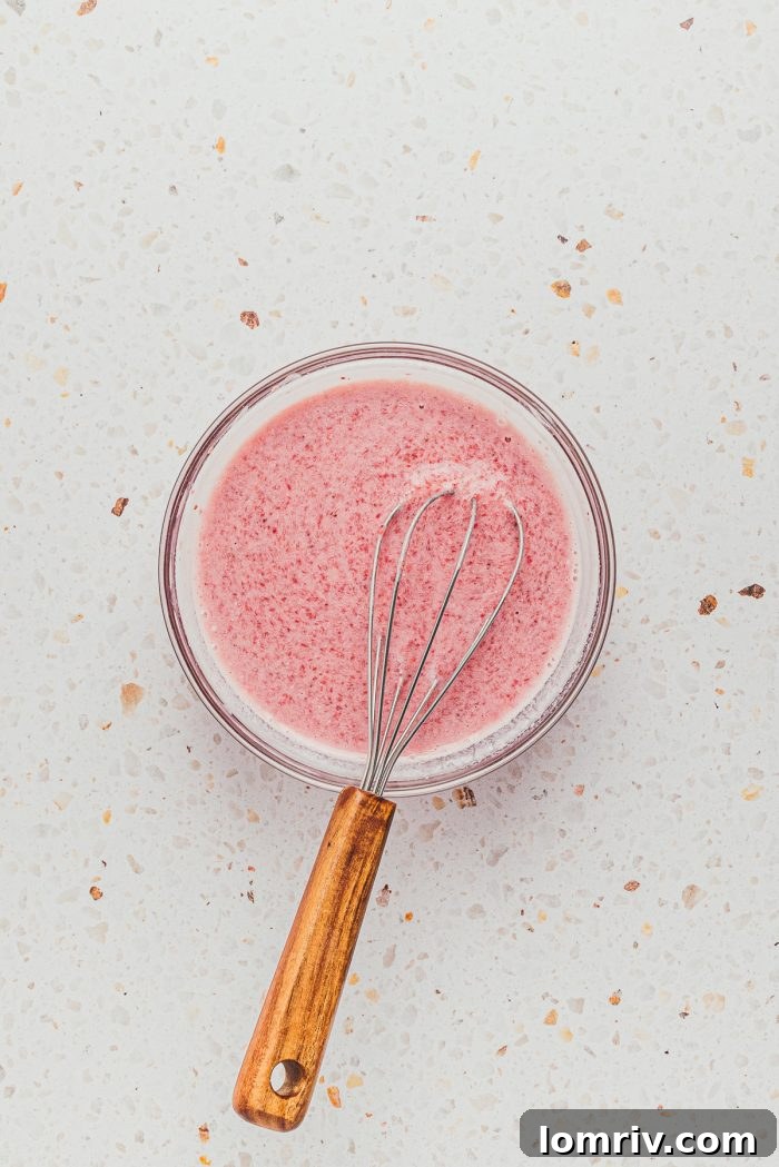 A bowl of wet ingredients for strawberry sheet cake, with a whisk nearby, ready for mixing