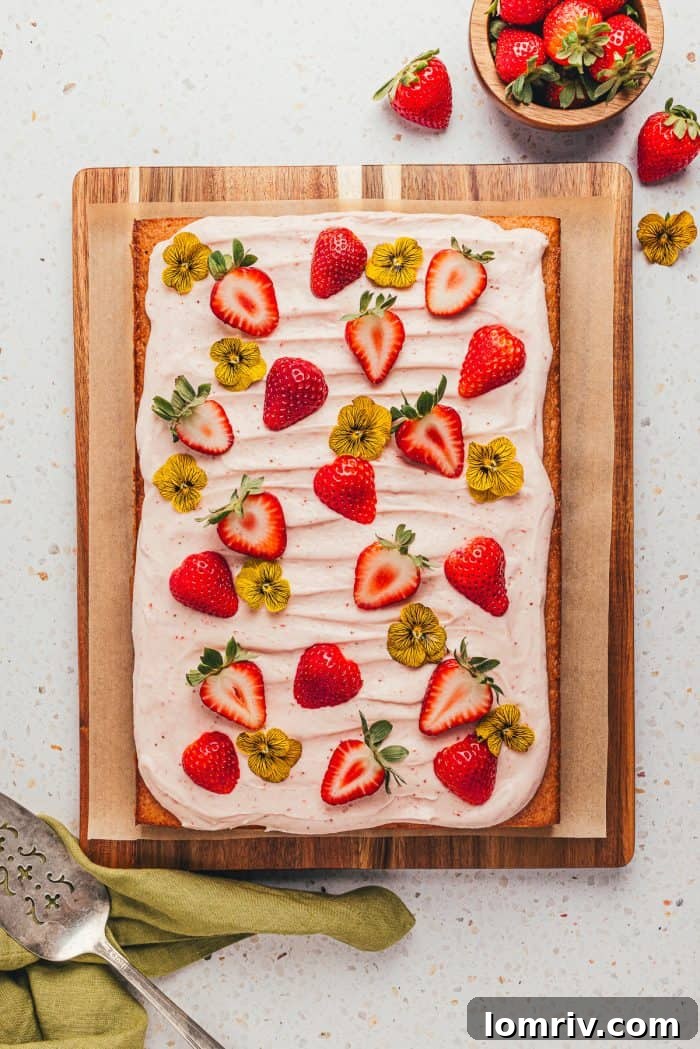A fully decorated strawberry sheet cake, adorned with fresh strawberries and edible flowers, ready to serve