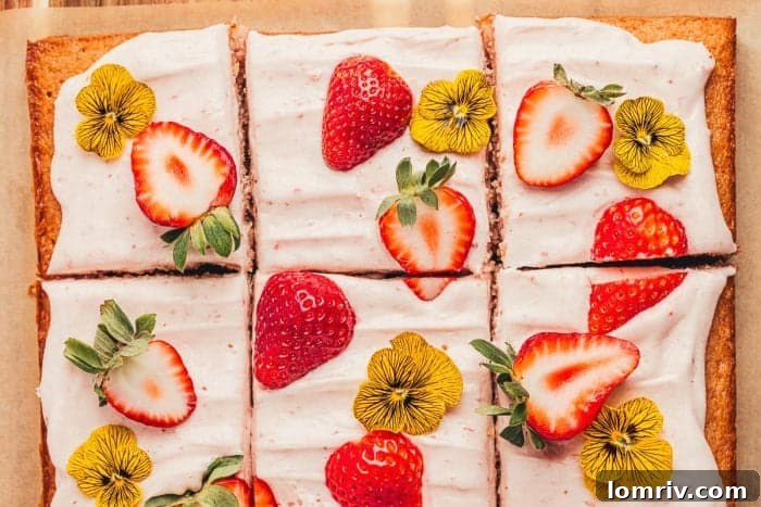 A close-up view of a beautifully decorated strawberry sheet cake, sliced and presented on a rustic wooden cutting board