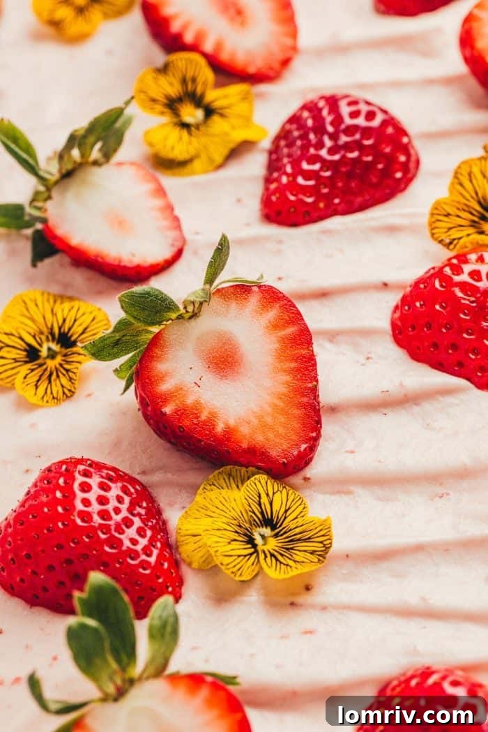 A captivating close-up of the delicate edible flowers and fresh strawberries adorning a strawberry sheet cake