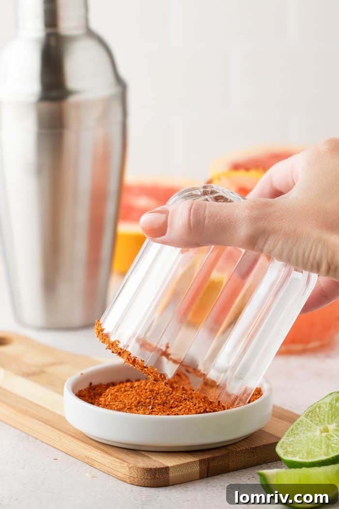 A cocktail glass being carefully dipped into a plate of vibrant Tajín seasoning to create a perfect rim.