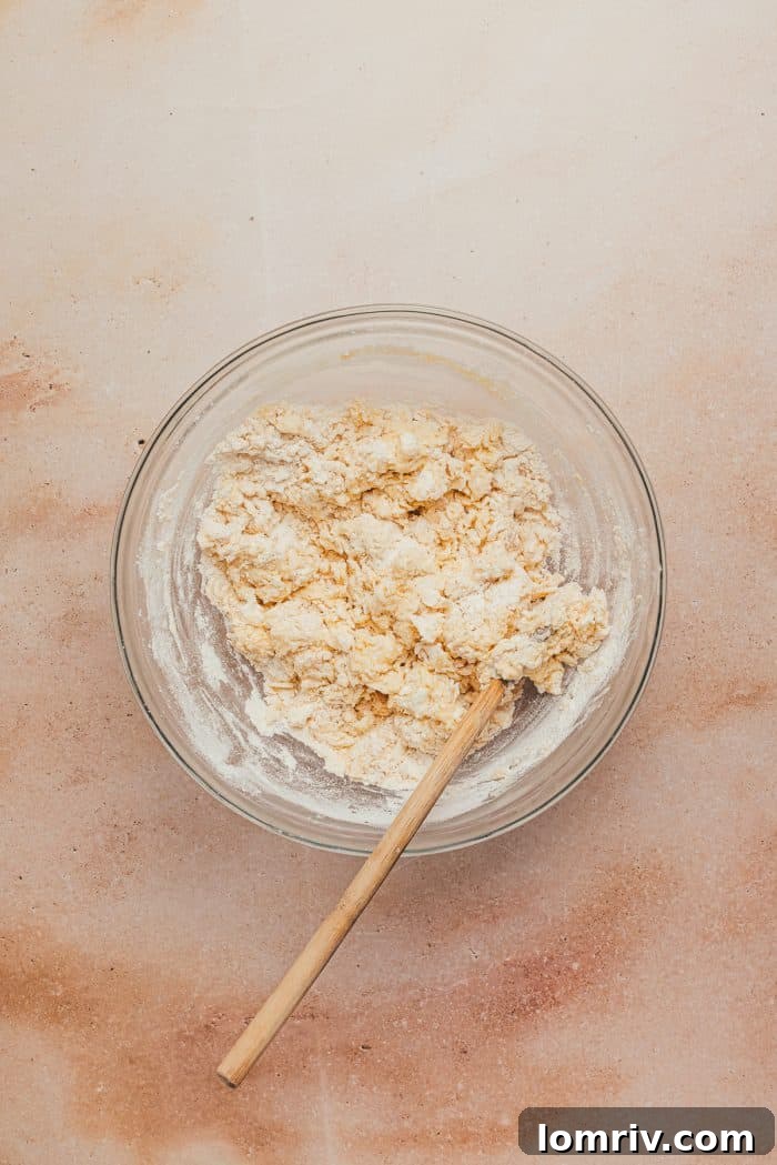 Scone dough being mixed with a spatula in a glass bowl, showcasing a crumbly texture.