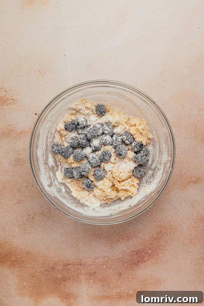 Scone dough with blackberries gently folded in, inside a glass mixing bowl.