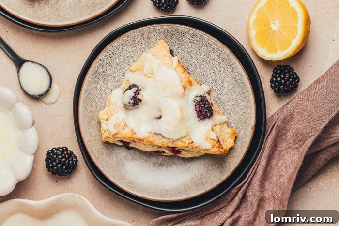 A charming close-up of a single glazed blackberry scone on a white plate.