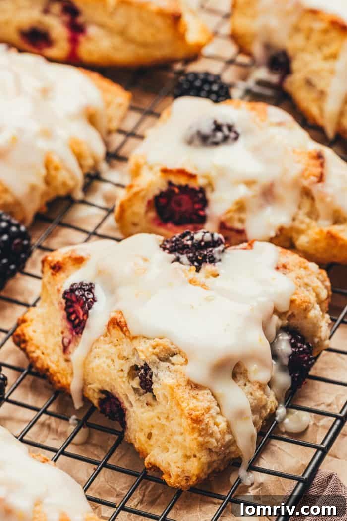 Several glazed blackberry buttermilk scones arranged on a cooling rack.