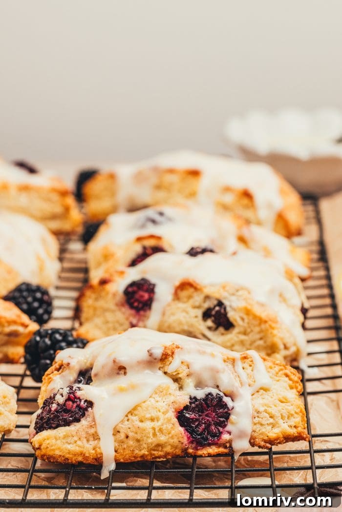 Close-up of glazed blackberry scones on a cooling rack, showing their flaky texture.
