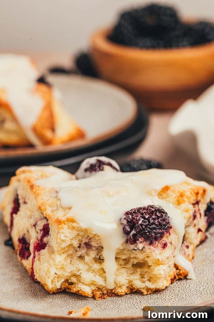 A glazed blackberry scone on a plate with a bite taken out, revealing its soft interior.