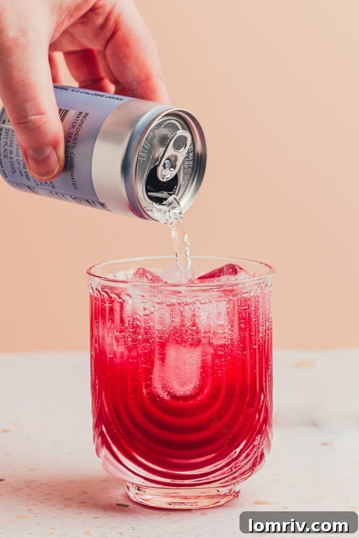 A blueberry cocktail in a glass being topped off with chilled club soda, creating a fizzy layer.