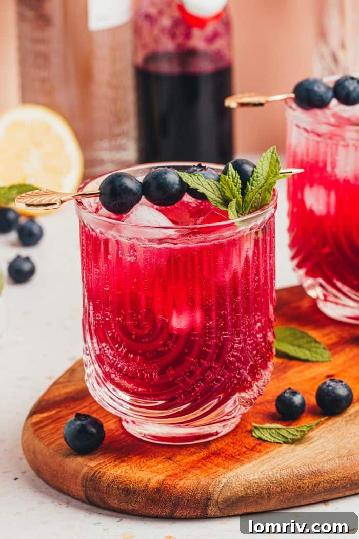 A hand reaching for a blueberry gin fizz cocktail on a table, highlighting its inviting appeal.