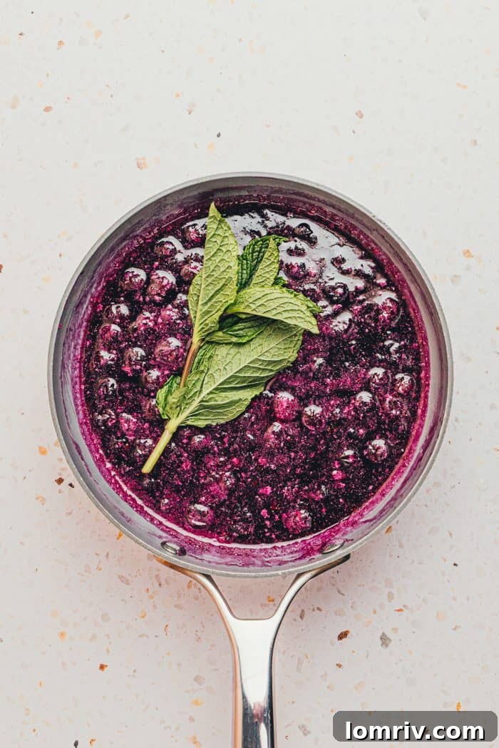 Cooked blueberry syrup in a saucepan, with a sprig of fresh mint submerged for infusion.