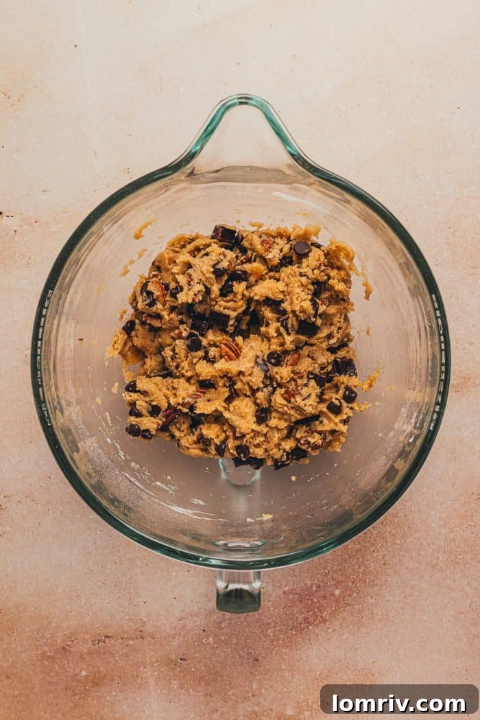 Chocolate chips mixed into the cookie dough in a glass mixing bowl.